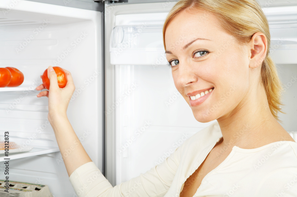 微笑的金发女郎从冰箱里拿出一个西红柿