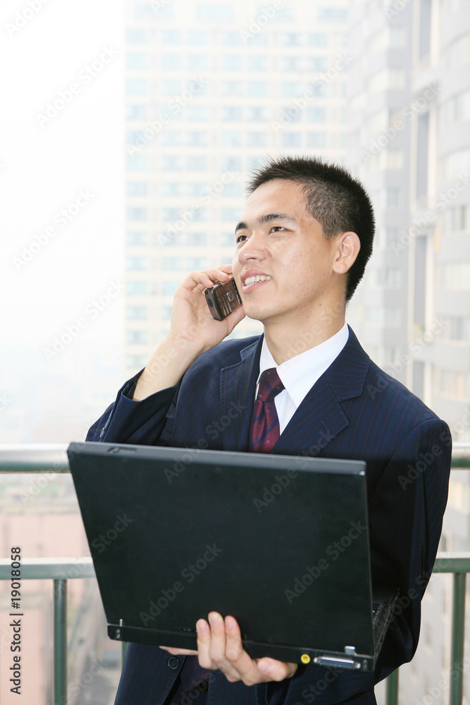 年轻的亚洲商人在阳台上听电话
