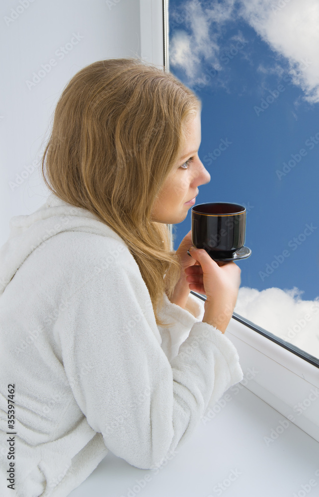 年轻漂亮的女孩在窗户边喝咖啡