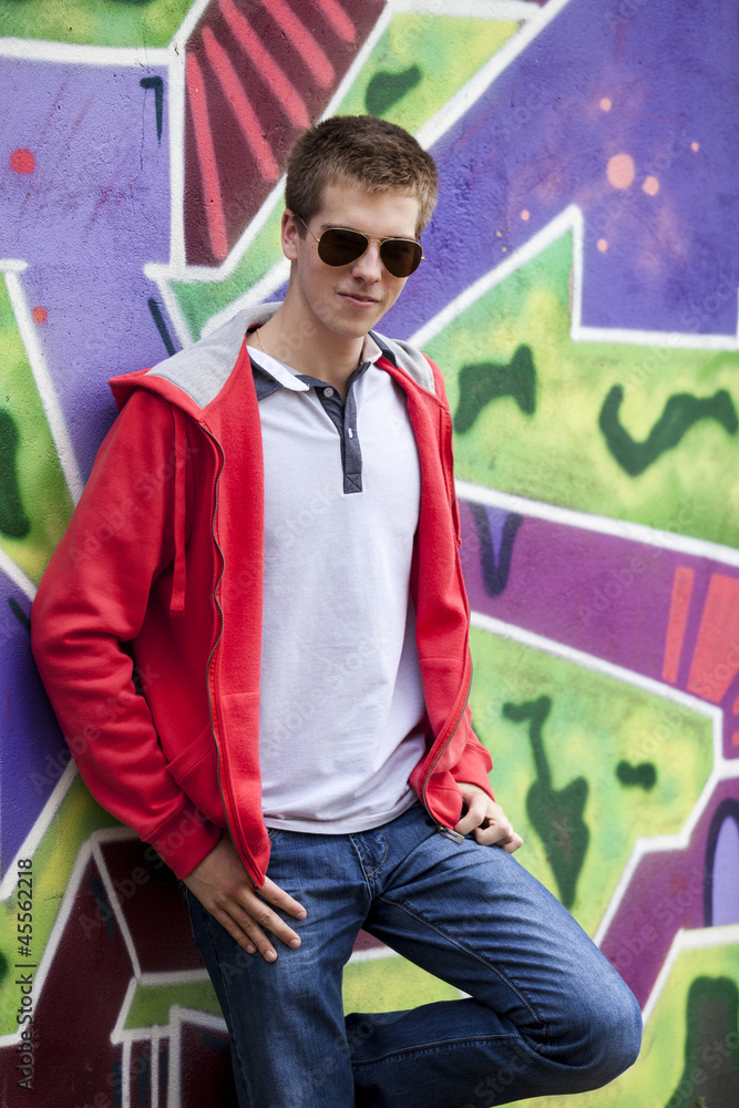 戴着眼镜的青少年站在涂鸦墙附近。