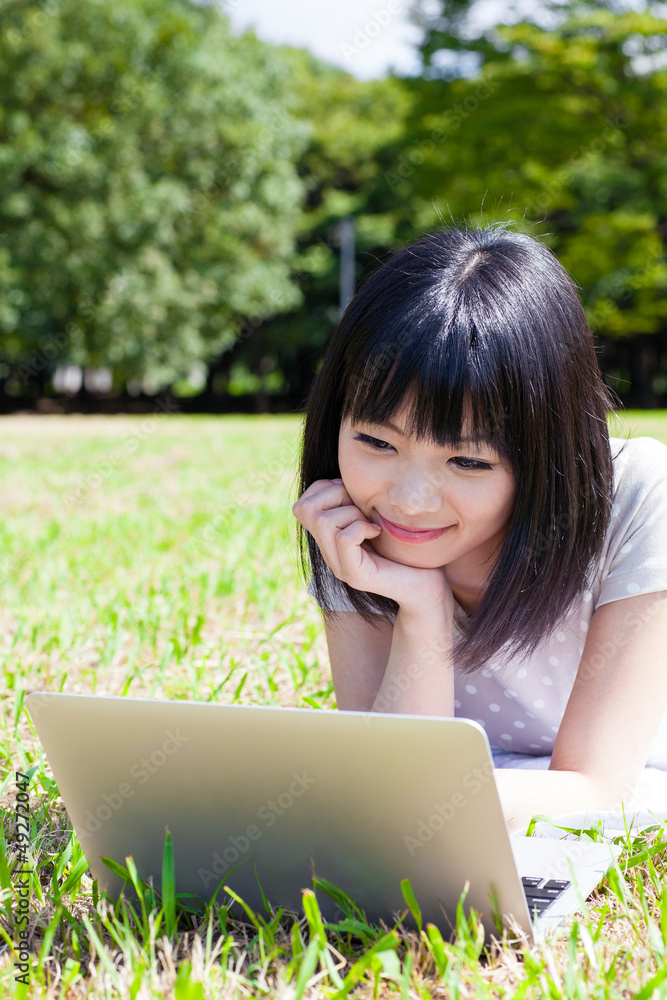 在公园里使用笔记本电脑的亚洲美女