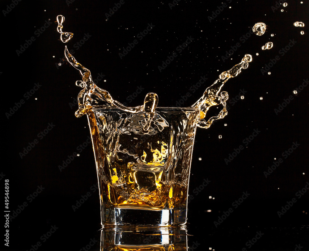 一杯带有飞溅物的威士忌，在黑色背景上隔离