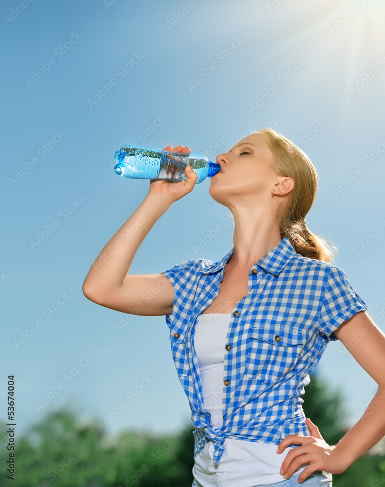 女人在夏天的户外用瓶子喝水