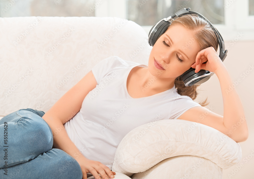 戴着耳机的女人躺在家里的沙发上欣赏音乐