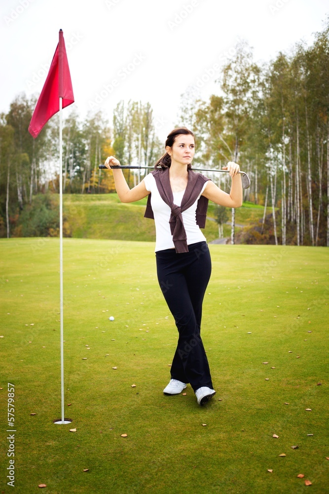 年轻女子高尔夫球手拿着球杆在果岭上摆姿势