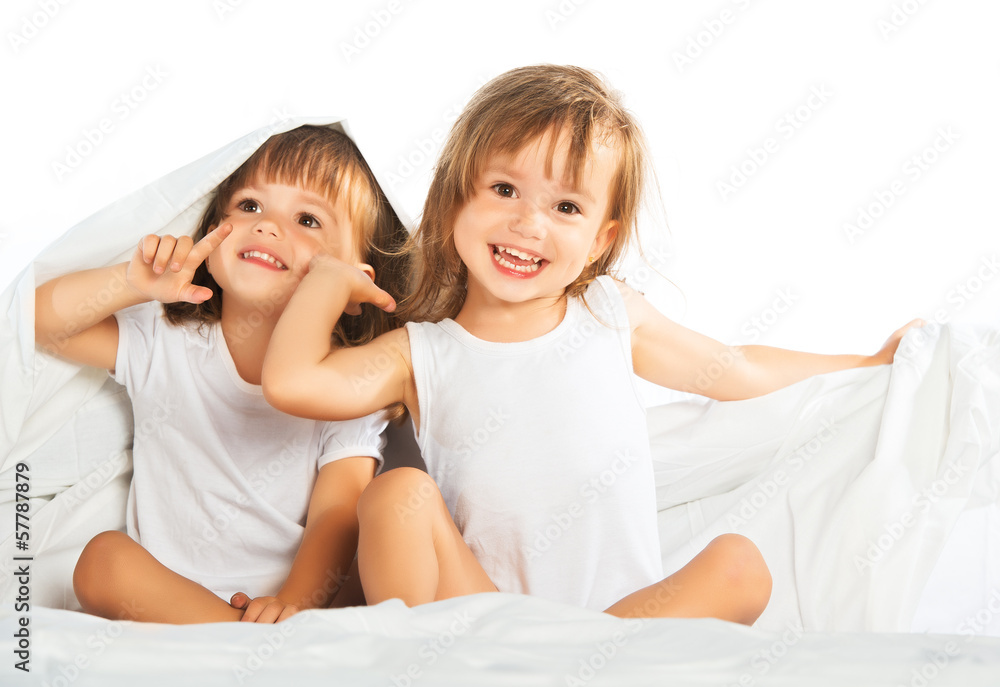快乐的小女孩双胞胎妹妹躺在床上的毯子下