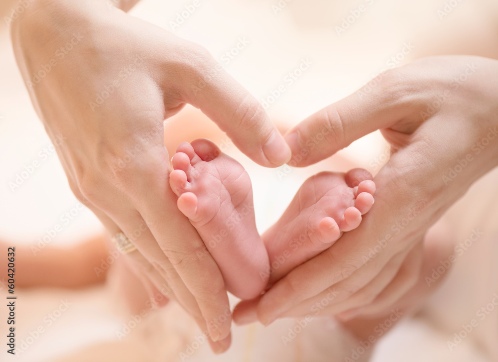 Tiny Newborn Baby feet on female Heart Shaped hands closeup