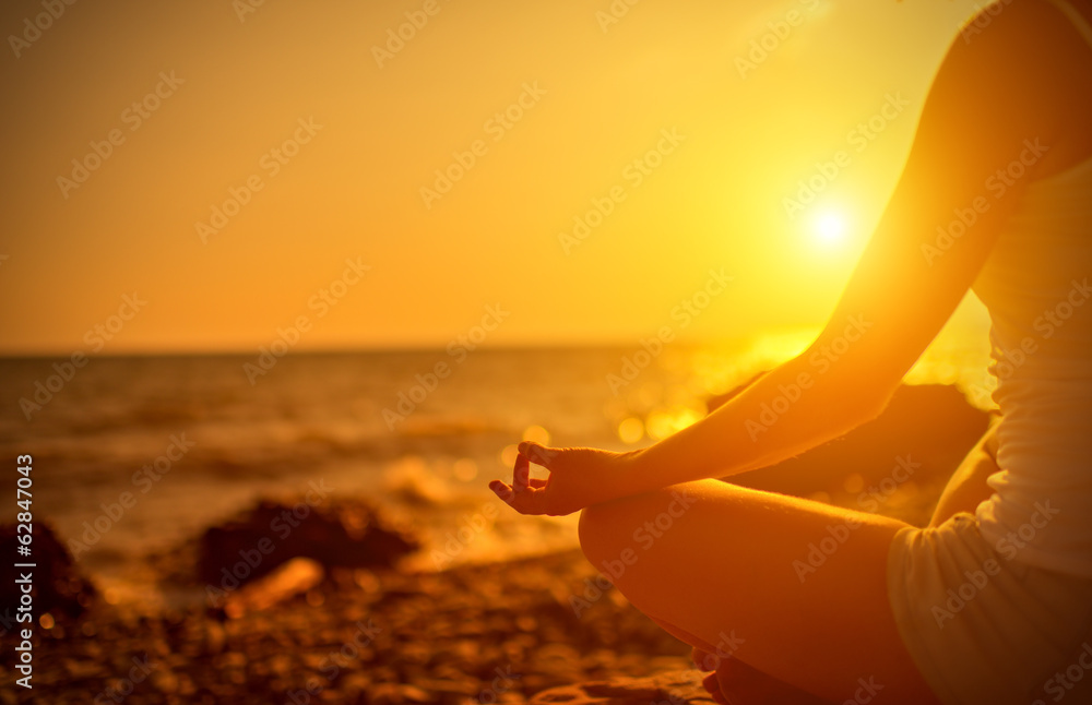 日落时在海滩上以瑜伽姿势冥想的女人的手
