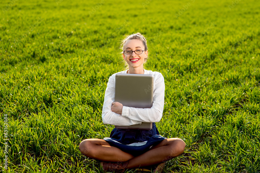 年轻微笑的女人，在绿地或公园里拿着笔记本电脑的女孩