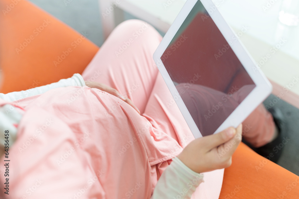 快乐的孕妇看着相机，使用数字平板电脑