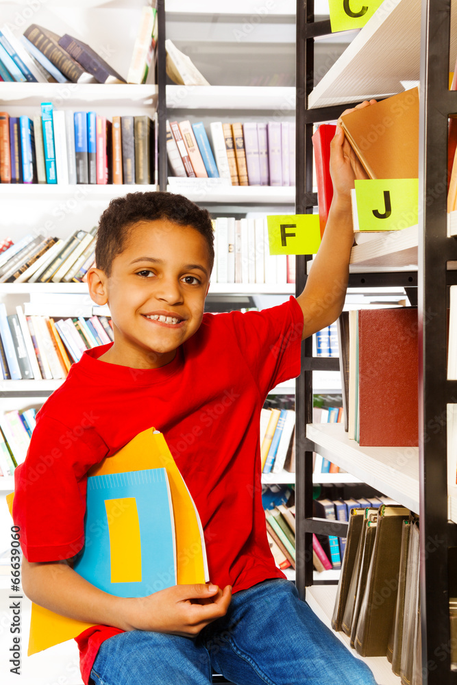 微笑的男孩把手放在书架上拿着书