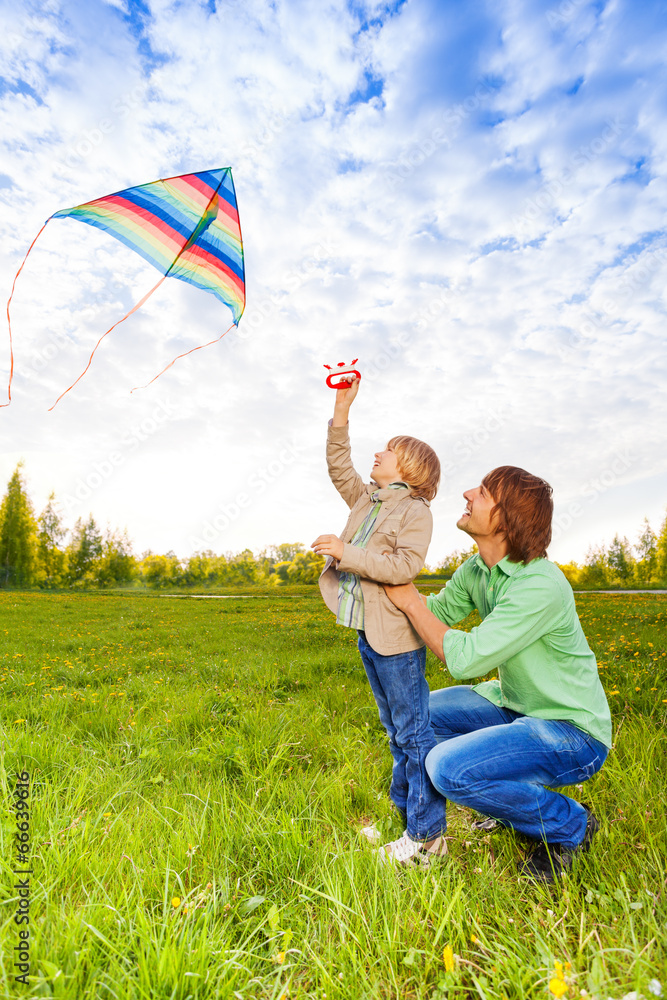 Father holds kid while watching flying kite
