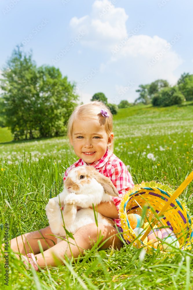 微笑的小女孩在绿色草地上拥抱兔子