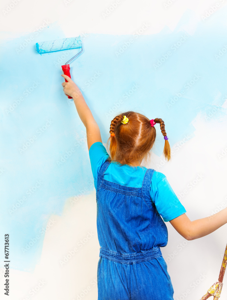穿着蓝色围兜和背带的小女孩在墙上画画