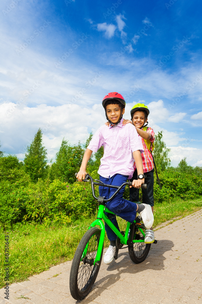 两个快乐的男孩骑着同一辆自行车，都站着