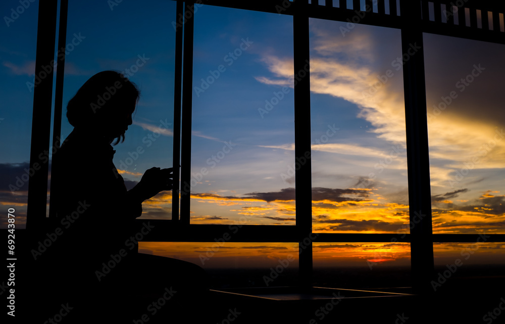 黄昏时分，黄昏时分，女孩在窗户边玩智能手机