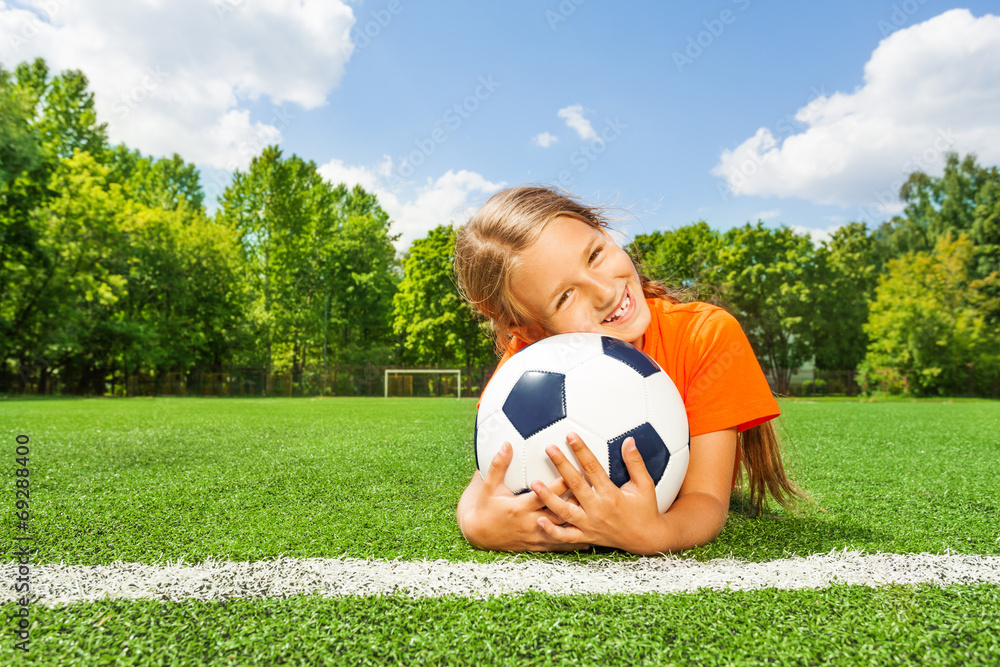 女孩紧紧抱着足球，微笑着躺着