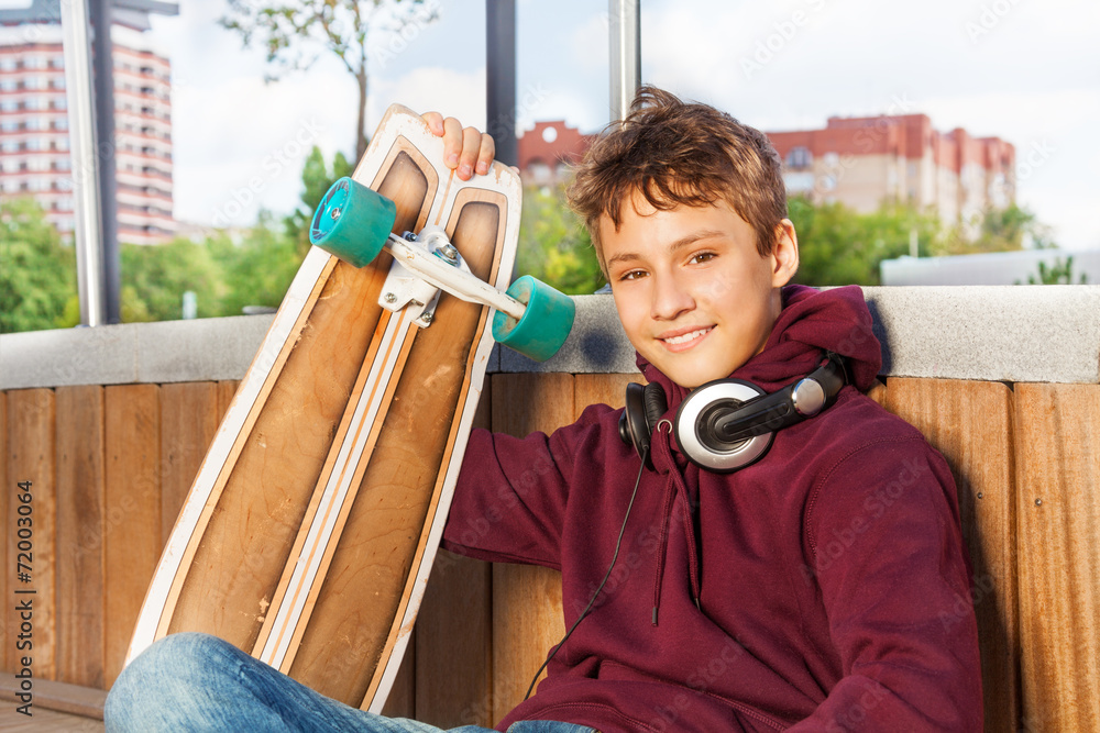 Positive cute boy holds skateboard while sitting