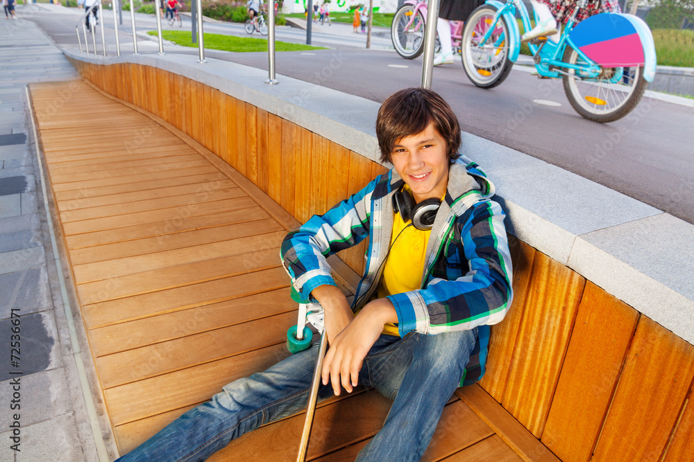 微笑男孩坐着，手臂放在膝盖上，拿着滑板
