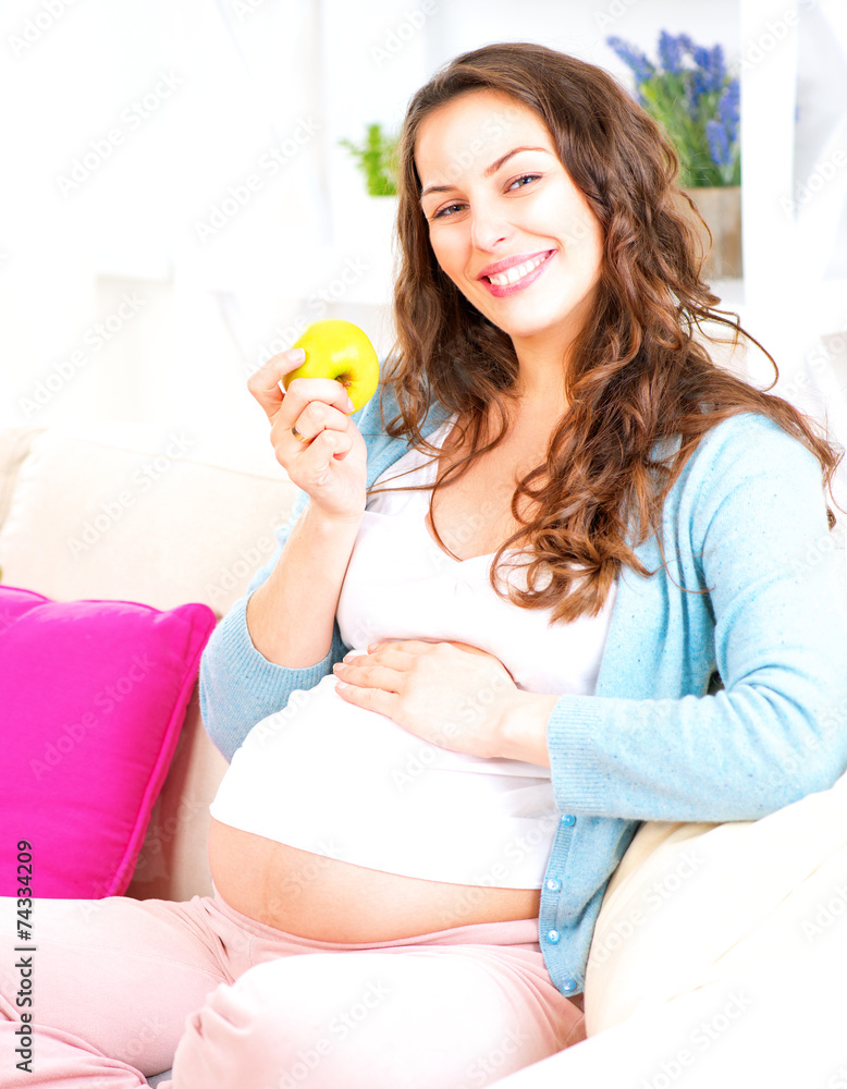 怀孕快乐的女人坐在沙发上吃苹果