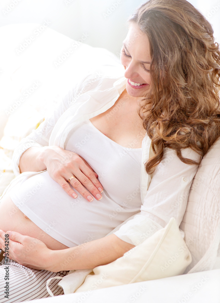 怀孕的微笑女人坐在沙发上抚摸她的肚子