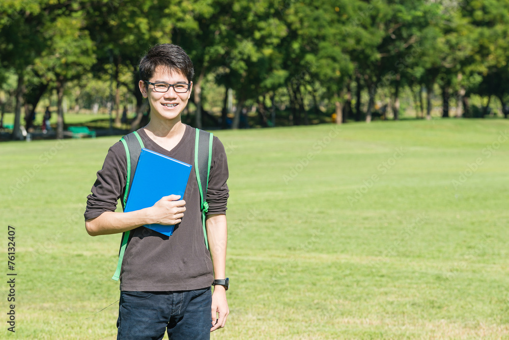 亚洲学生拿着书站在公园a微笑