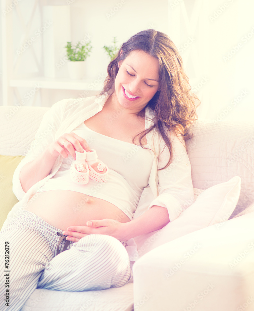 Pregnant happy woman holding baby shoes in her hands