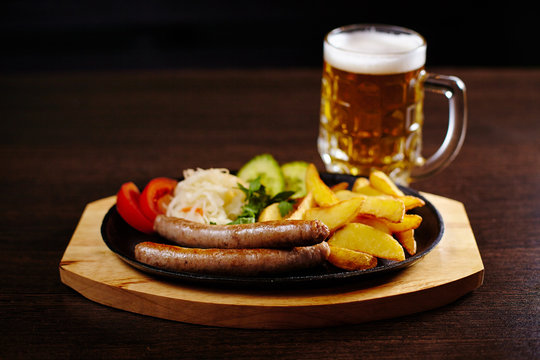 Roasted sausages in a frying pan on wooden table with beer