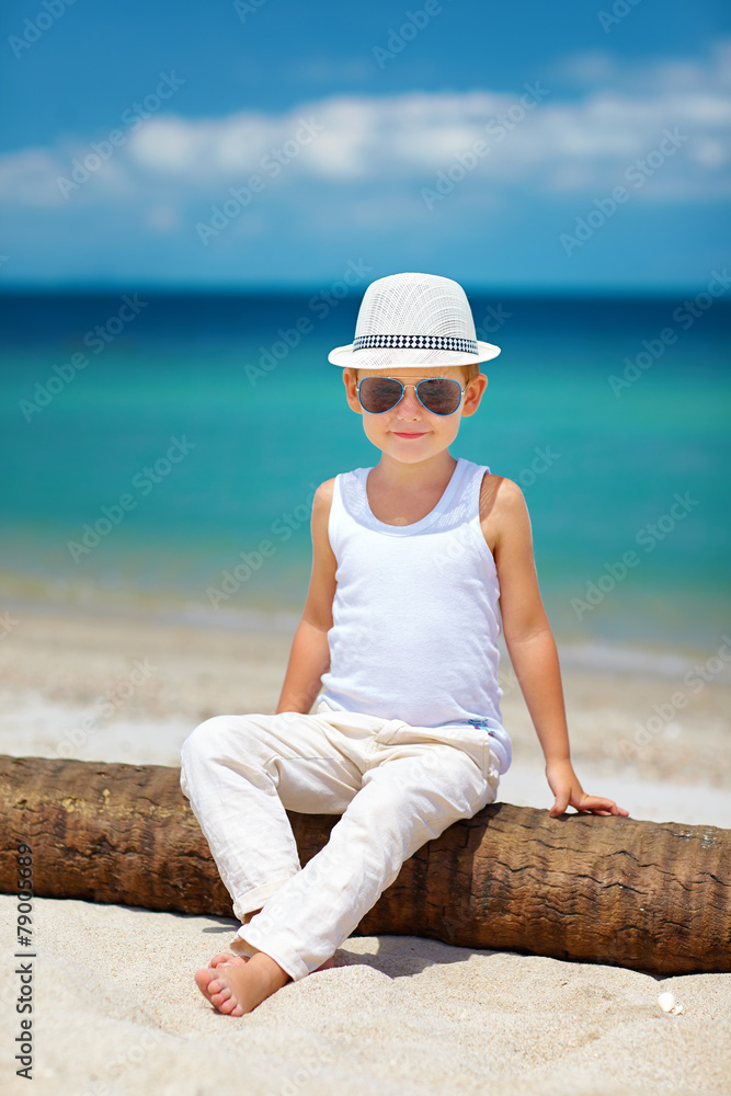 时尚小男孩坐在海滩的棕榈树上