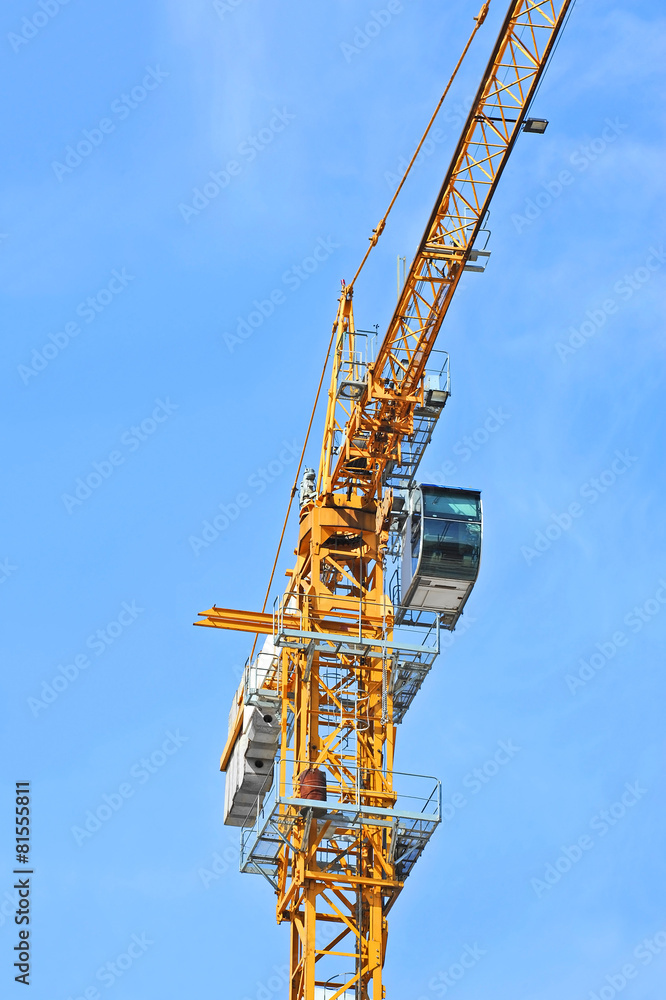 Yellow construction tower crane against blue sky