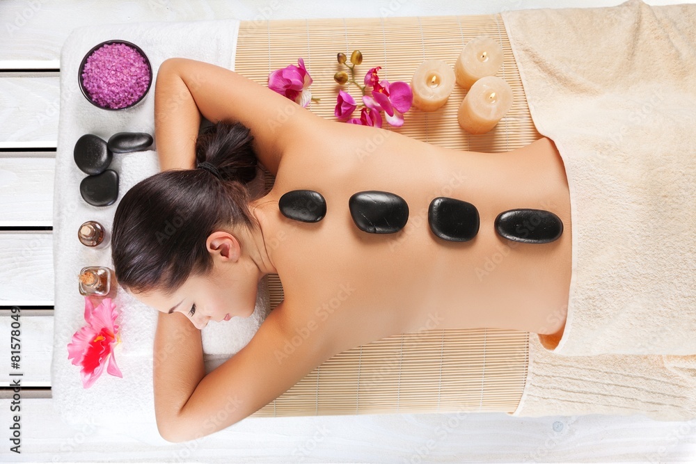 Adult. Adult woman relaxing in spa salon with hot stones on body