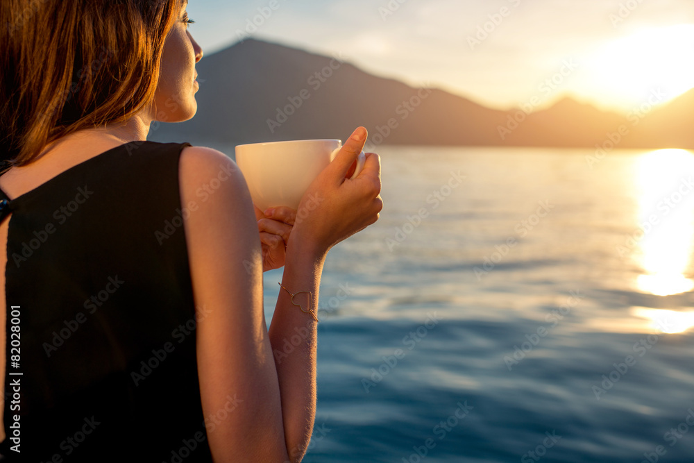 Young woman drinking coffee on the pier at sunrise