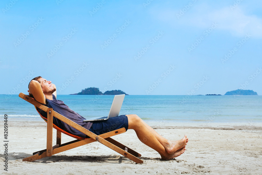 带着电脑微笑的商人在海滩上放松