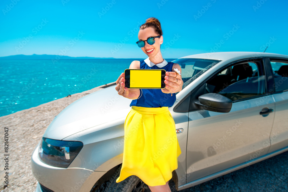 一名女子在汽车附近展示手机屏幕