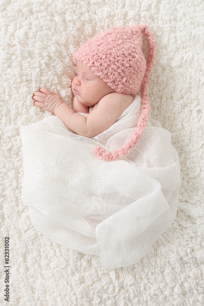 新生女婴戴着一顶粉色帽子，裹着复古蕾丝。