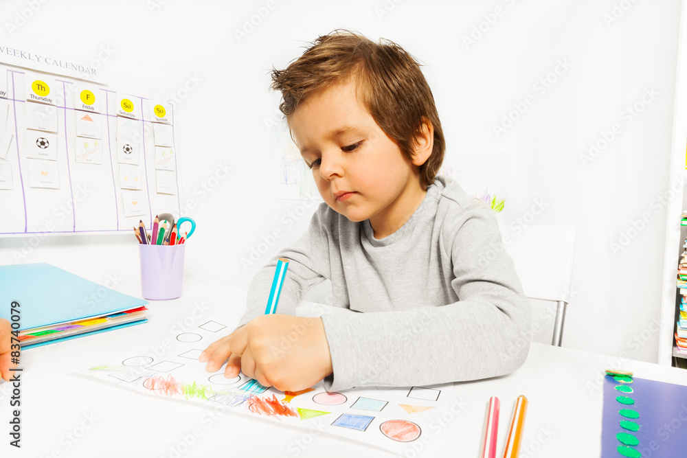 小男孩坐着用铅笔在纸上画画