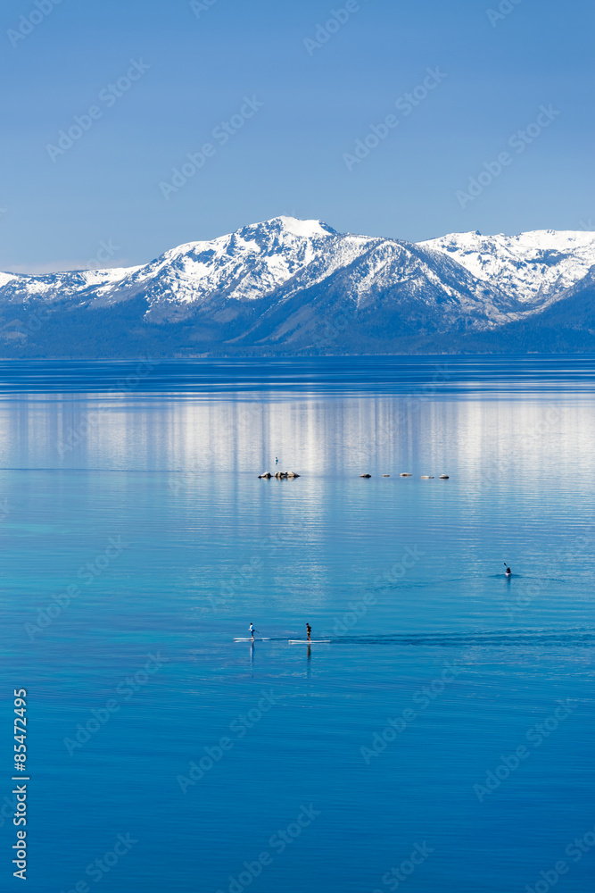 两个桨板和皮划艇在平静的太浩湖上，可以看到内华达山脉的雪山。