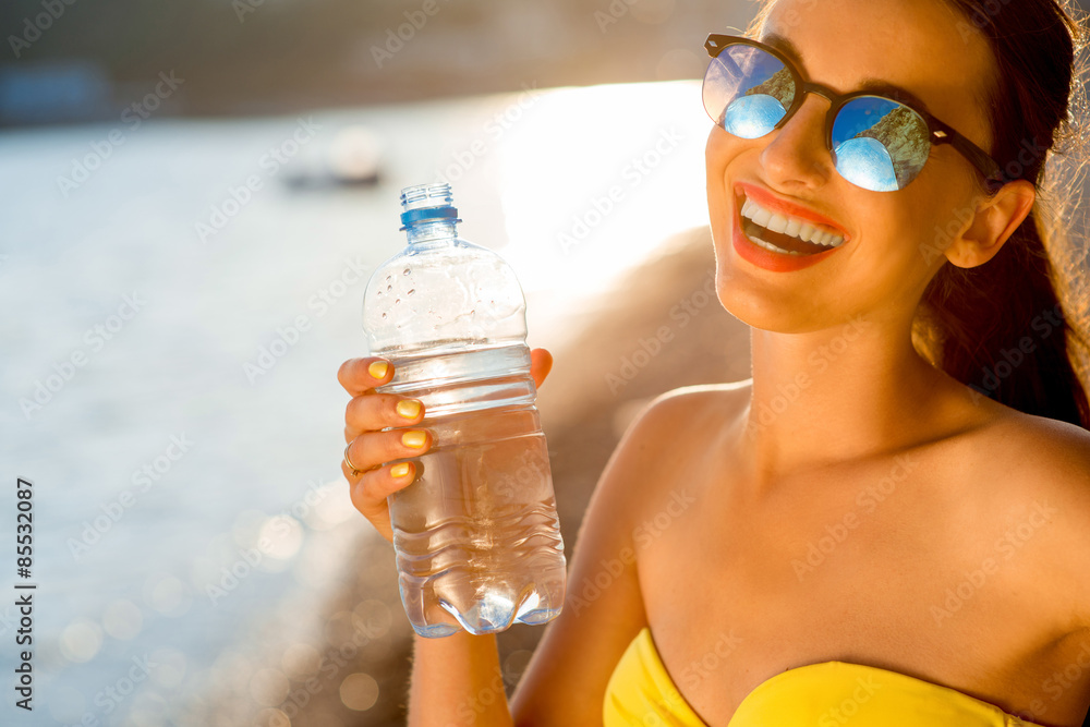 海滩上用透明瓶喝水的女人
