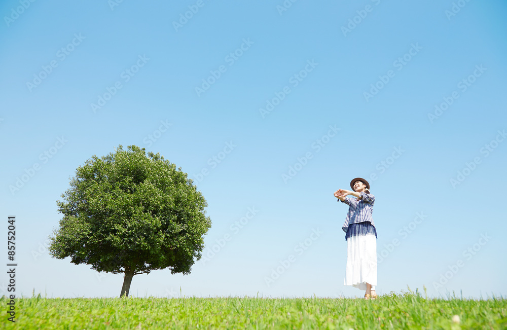 一本木のある原っぱに立つ女性