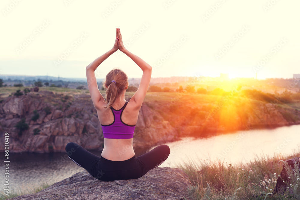 Young woman practicing yoga on the hill at sunset