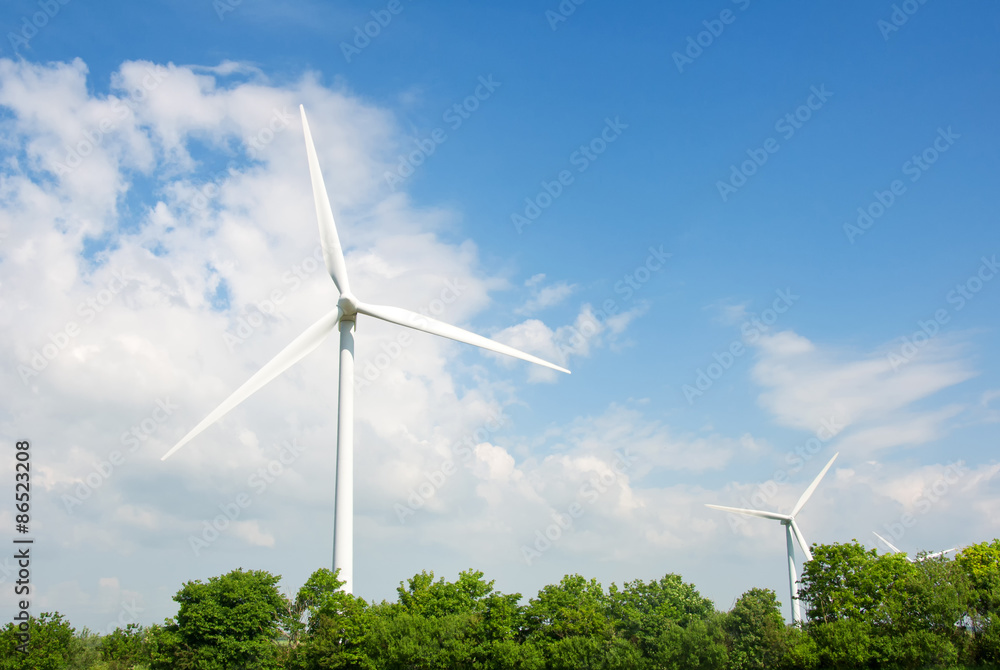 Wind turbines with blue sky and green tree tops