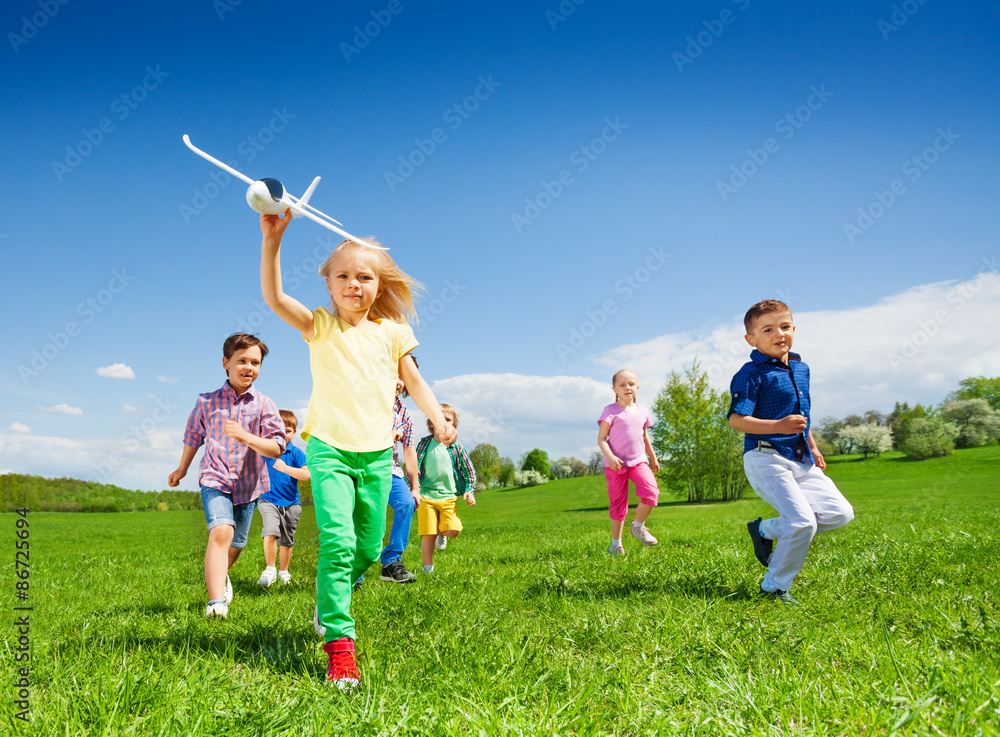 Small girl runs with kids and holds airplane toy