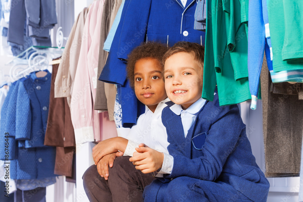 两个小男孩坐在衣架上的衣服旁边