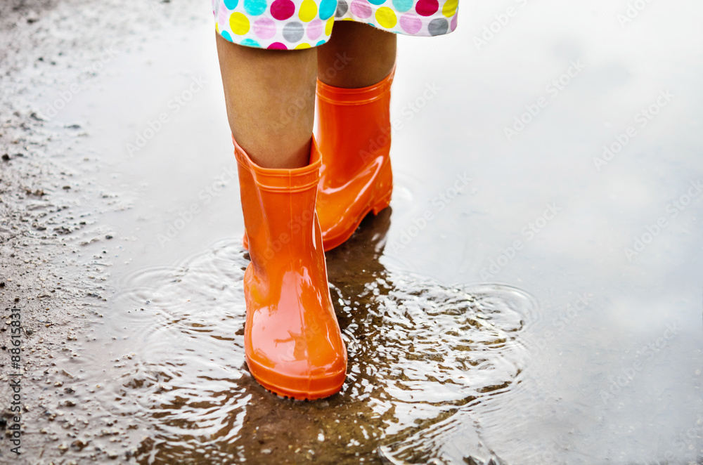 穿着橙色雨靴的孩子走进水坑。特写
