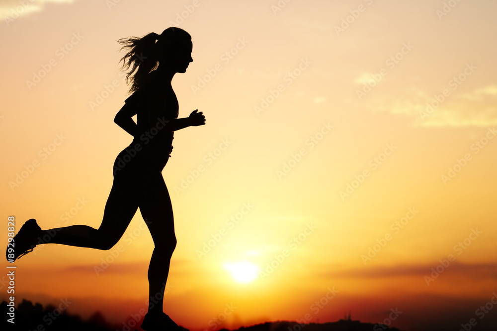 日落时女性慢跑者的剪影。