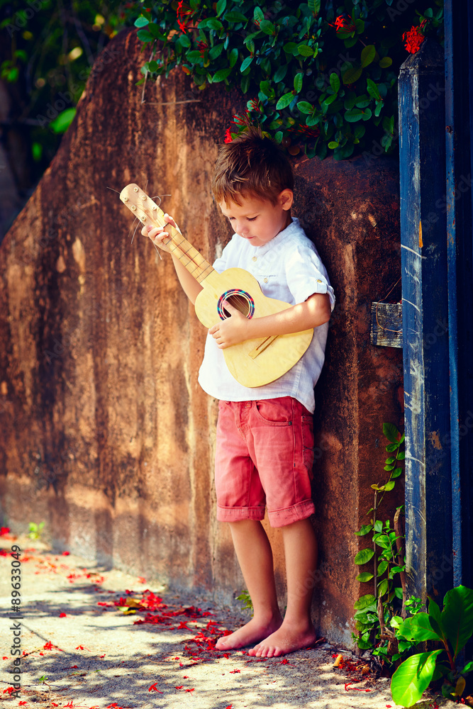 可爱的小男孩在夏天的旧篱笆附近弹吉他