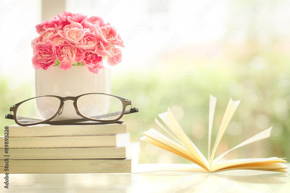 清新的粉红色康乃馨花，背景为书籍和眼镜