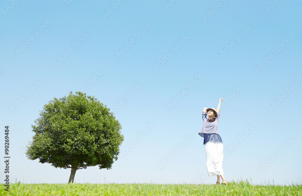 一本木のある原っぱに立つ女性　背伸び