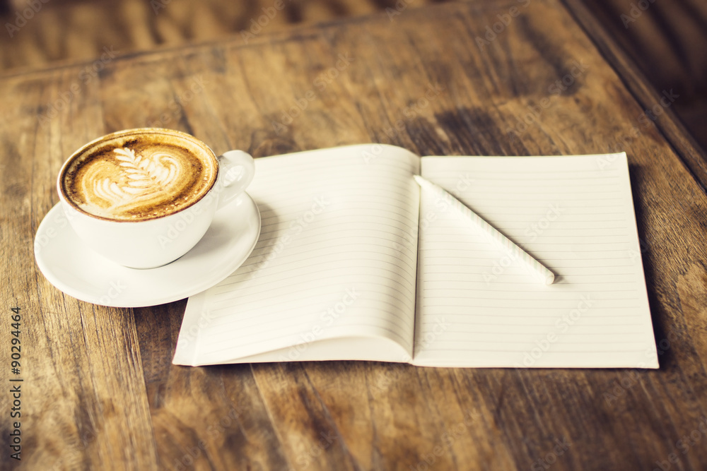 木桌上放着一杯咖啡和一本铅笔的空白日记