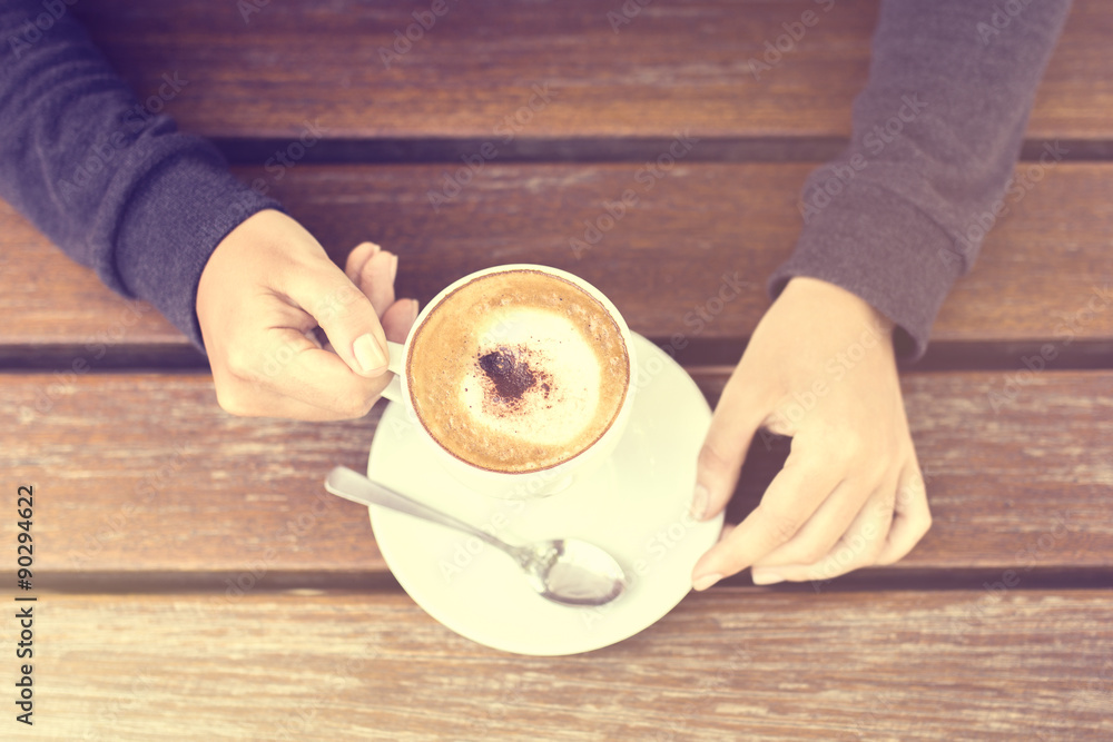 Girl holding a cup of cappuccino and wooden table